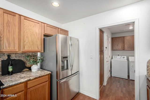 kitchen with stainless steel fridge, washing machine and dryer, dark hardwood / wood-style floors, tasteful backsplash, and light stone counters