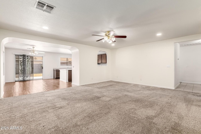 unfurnished living room featuring ceiling fan, light carpet, and a textured ceiling