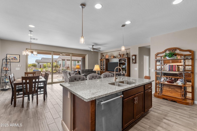 kitchen with light stone countertops, ceiling fan with notable chandelier, sink, dishwasher, and hanging light fixtures