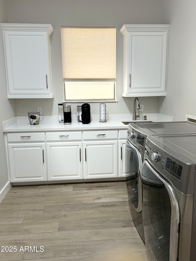 laundry area with washing machine and dryer, light wood-type flooring, cabinets, and sink