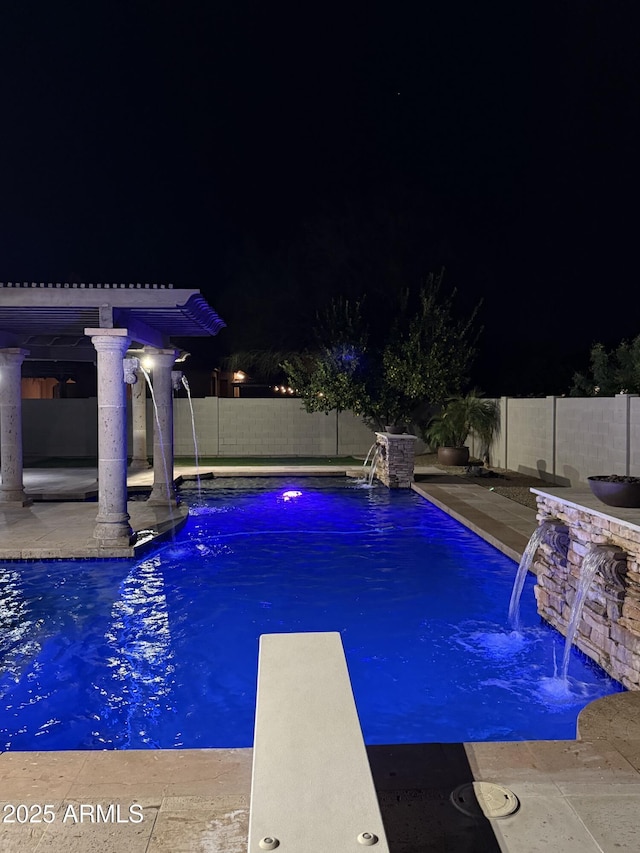 pool at twilight featuring a diving board and pool water feature