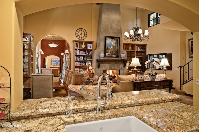 kitchen featuring a fireplace, decorative light fixtures, sink, a chandelier, and light stone countertops