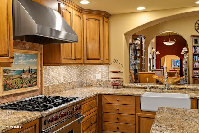 kitchen featuring sink, high end range, decorative backsplash, light stone counters, and wall chimney exhaust hood