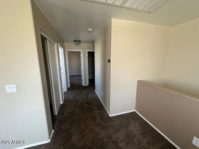 hallway featuring dark colored carpet and baseboards