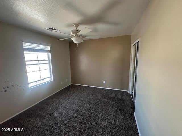 spare room featuring baseboards, visible vents, a ceiling fan, a textured ceiling, and dark carpet