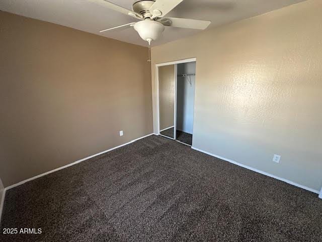 unfurnished bedroom with ceiling fan, baseboards, dark colored carpet, and a closet