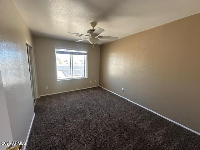 empty room featuring ceiling fan, baseboards, dark colored carpet, and a textured ceiling