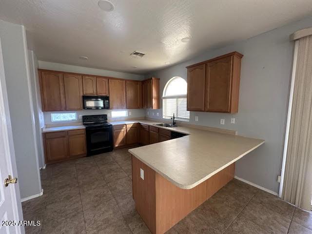 kitchen with a peninsula, a sink, light countertops, black appliances, and brown cabinetry