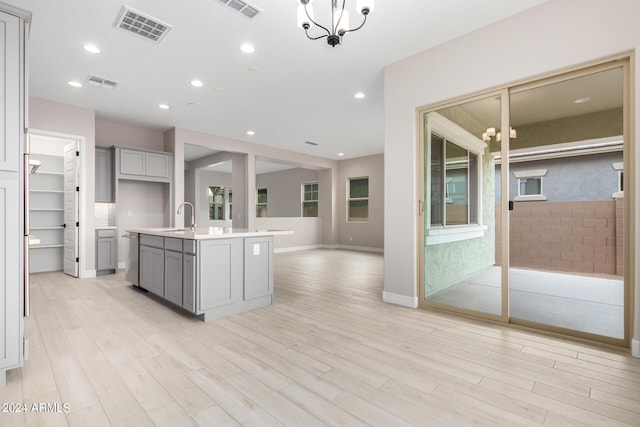 kitchen featuring wall chimney range hood, stainless steel appliances, sink, and a center island with sink