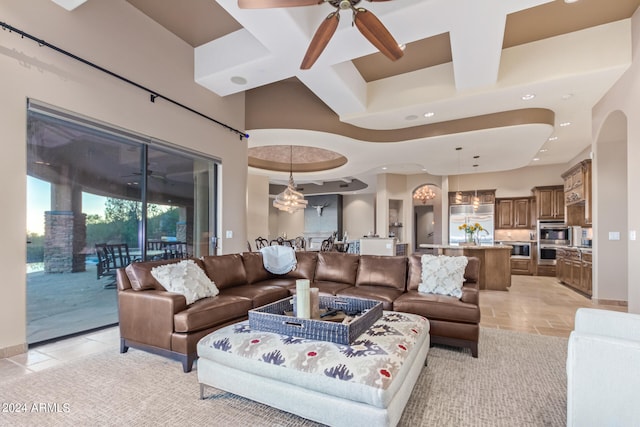 tiled living room with coffered ceiling, a high ceiling, and ceiling fan with notable chandelier