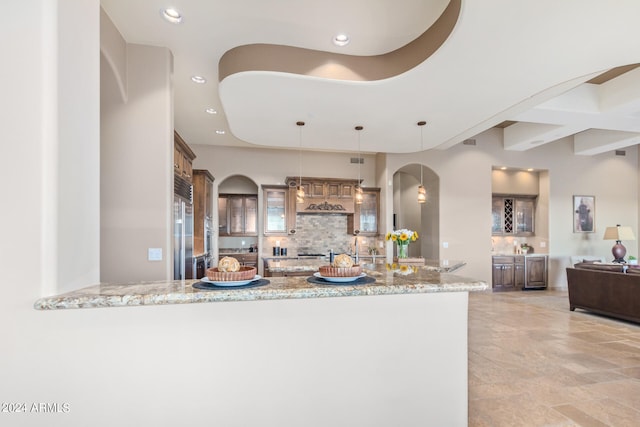 kitchen featuring light tile floors, decorative light fixtures, refrigerator, backsplash, and light stone counters