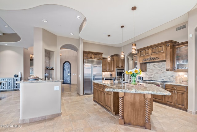 kitchen featuring backsplash, a kitchen island with sink, appliances with stainless steel finishes, light tile floors, and light stone counters