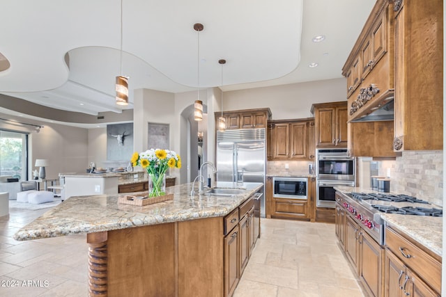 kitchen with backsplash, a center island with sink, sink, and built in appliances