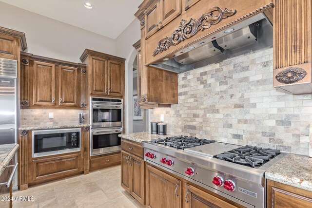 kitchen with light tile flooring, backsplash, custom exhaust hood, built in appliances, and light stone countertops