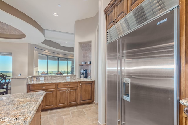 kitchen with built in refrigerator, light tile floors, and light stone counters