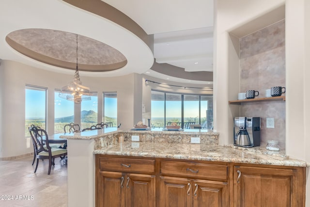 kitchen featuring light tile flooring, pendant lighting, light stone counters, a raised ceiling, and a chandelier