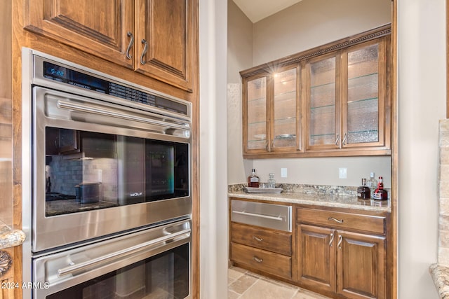 kitchen with double oven, light stone counters, and light tile floors