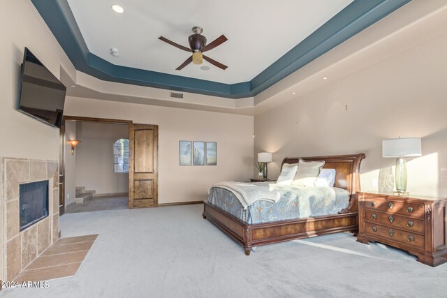 carpeted bedroom with a fireplace, ceiling fan, and a tray ceiling