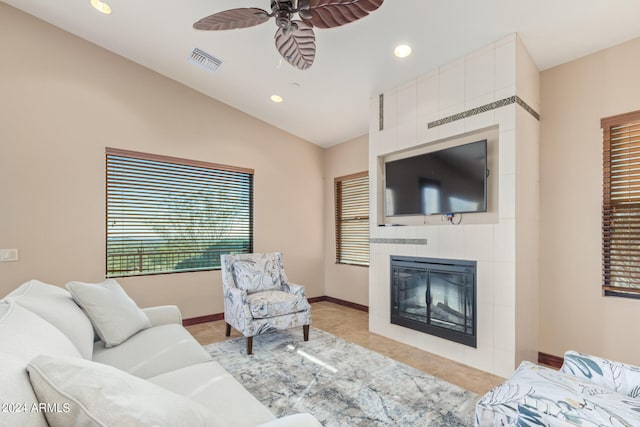 living room with a tiled fireplace, lofted ceiling, ceiling fan, and light tile floors