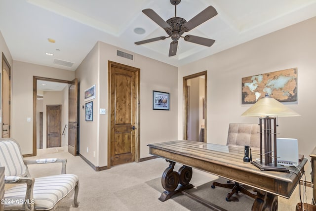 carpeted home office with ceiling fan and a raised ceiling