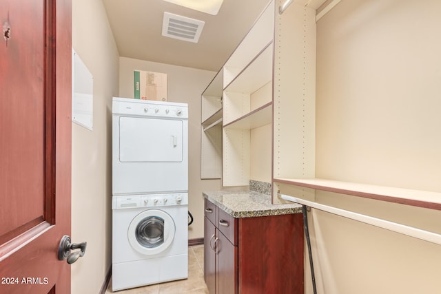 laundry room with stacked washer / dryer, cabinets, and light tile flooring