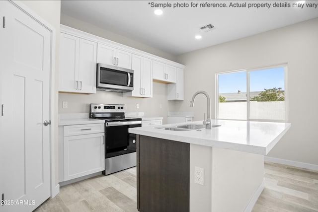 kitchen with an island with sink, sink, white cabinets, light hardwood / wood-style floors, and stainless steel appliances