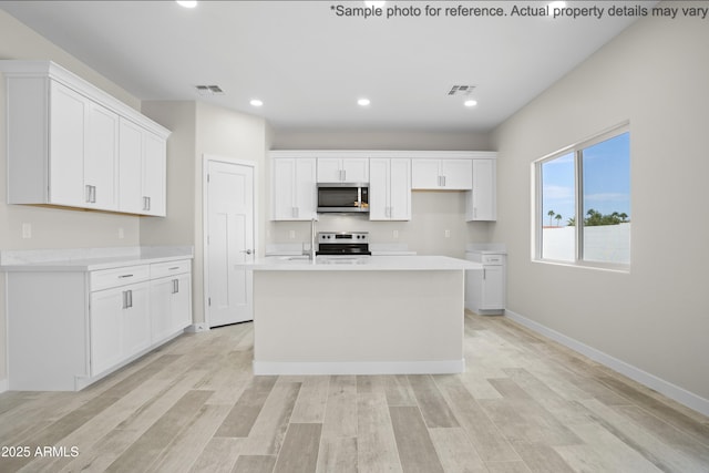 kitchen with white cabinetry, appliances with stainless steel finishes, an island with sink, and light hardwood / wood-style flooring