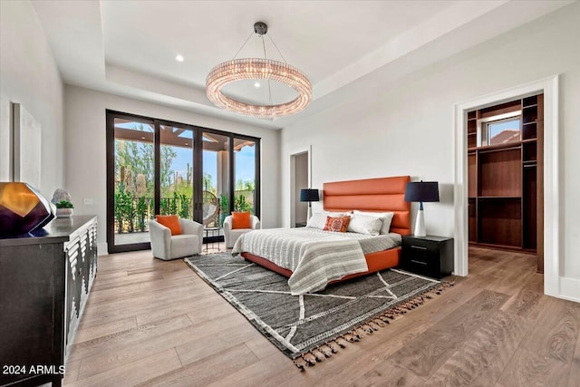 bedroom with a walk in closet, a tray ceiling, light hardwood / wood-style floors, and access to outside