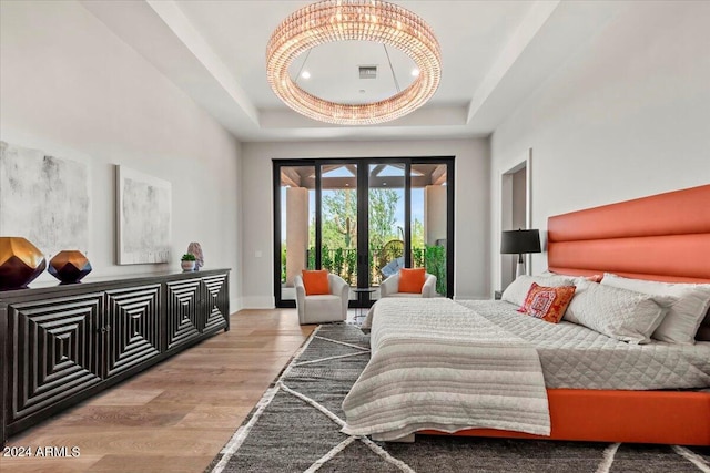 bedroom with french doors, access to exterior, light hardwood / wood-style floors, and a tray ceiling