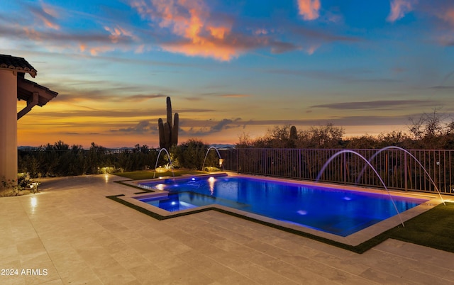 pool at dusk featuring an in ground hot tub, pool water feature, and a patio area