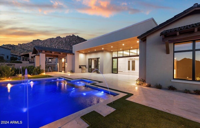 pool at dusk featuring a patio and pool water feature