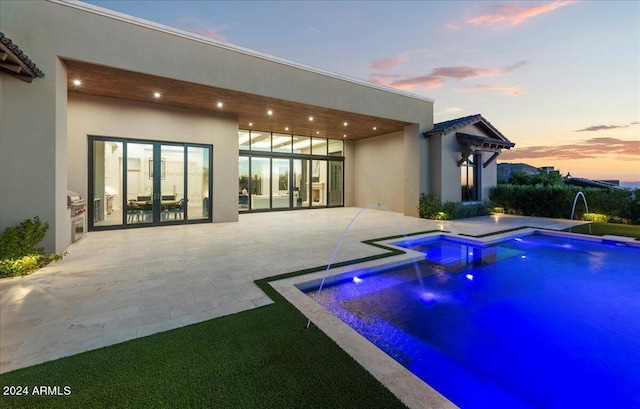 pool at dusk with pool water feature, a hot tub, and a patio area