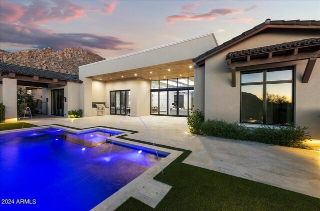 back house at dusk with pool water feature, a swimming pool with hot tub, and a patio