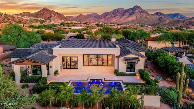 back house at dusk featuring a mountain view and a patio