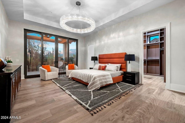 bedroom featuring access to exterior, a tray ceiling, a spacious closet, french doors, and light wood-type flooring