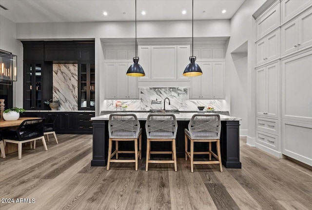 kitchen with white cabinetry, decorative light fixtures, and a center island with sink