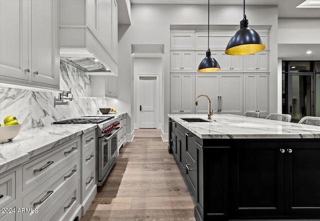 kitchen with decorative light fixtures, white cabinetry, sink, range with two ovens, and a large island with sink