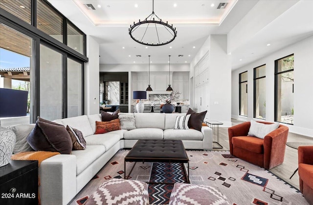 living room with a towering ceiling, a raised ceiling, light hardwood / wood-style floors, and a notable chandelier