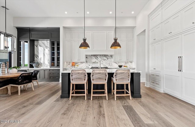 kitchen featuring decorative backsplash, an island with sink, white cabinets, decorative light fixtures, and light wood-type flooring