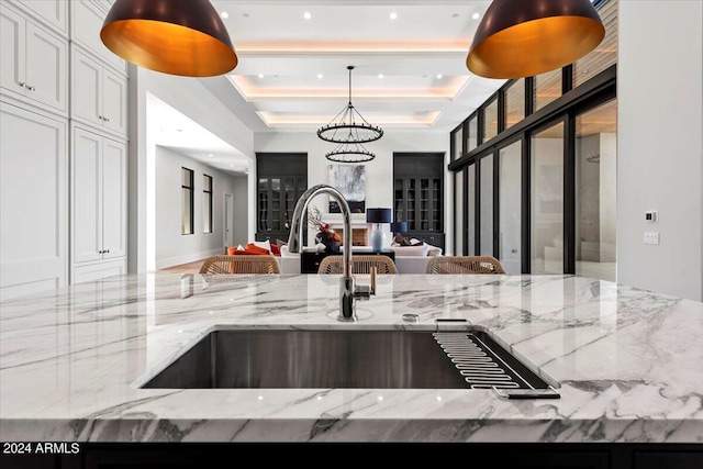 kitchen featuring sink, a breakfast bar area, light stone countertops, white cabinets, and a raised ceiling