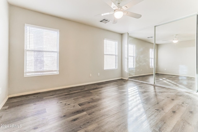 unfurnished bedroom featuring multiple windows, hardwood / wood-style floors, a closet, and ceiling fan