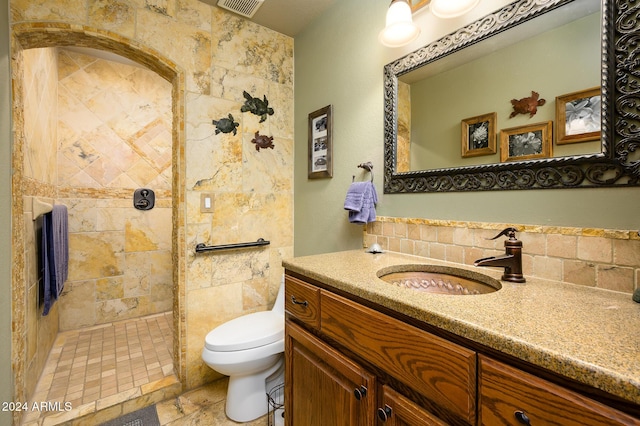 bathroom with a tile shower, vanity, tile walls, and toilet