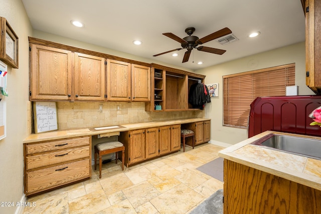 kitchen with ceiling fan, sink, built in desk, and backsplash