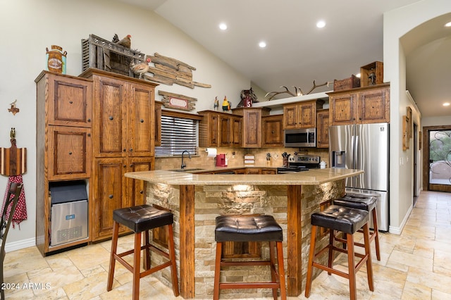 kitchen with a center island, a kitchen breakfast bar, vaulted ceiling, decorative backsplash, and appliances with stainless steel finishes