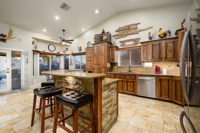 kitchen with decorative backsplash, stainless steel appliances, ceiling fan, sink, and a breakfast bar area