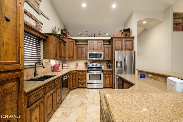 kitchen featuring light stone counters, sink, appliances with stainless steel finishes, and vaulted ceiling