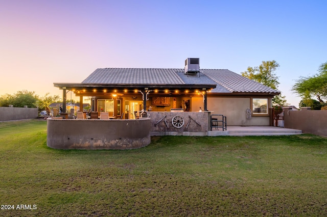 back house at dusk with exterior bar, a yard, cooling unit, and a patio area