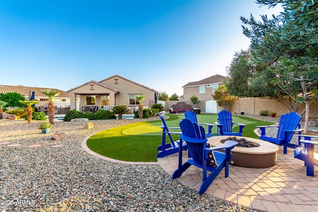 fenced backyard featuring a fire pit, a putting green, and a patio