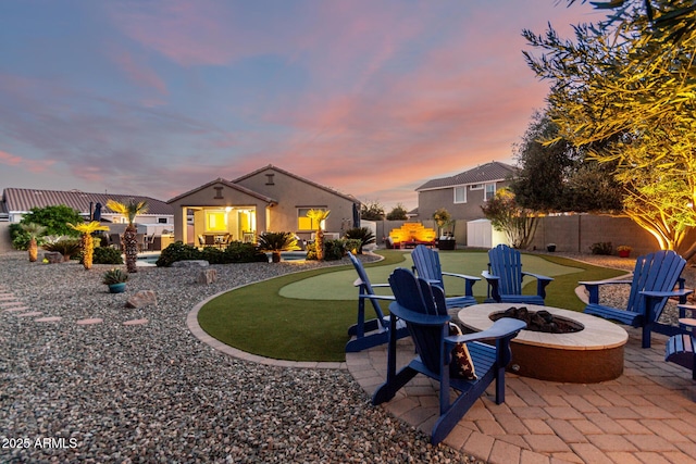 rear view of property featuring a putting area, an outdoor structure, a fire pit, a patio area, and a fenced backyard