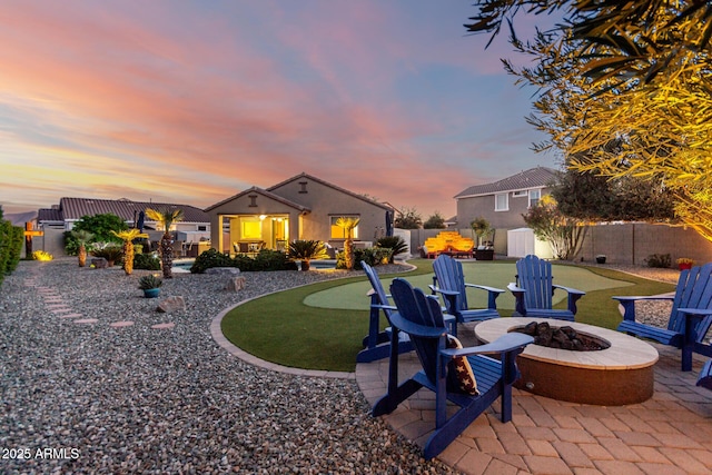 back of property at dusk with a putting green, an outdoor fire pit, an outbuilding, a patio, and a fenced backyard